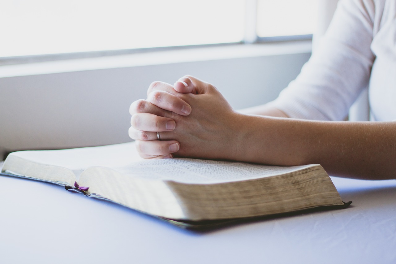 Praying hands resting on open Bible