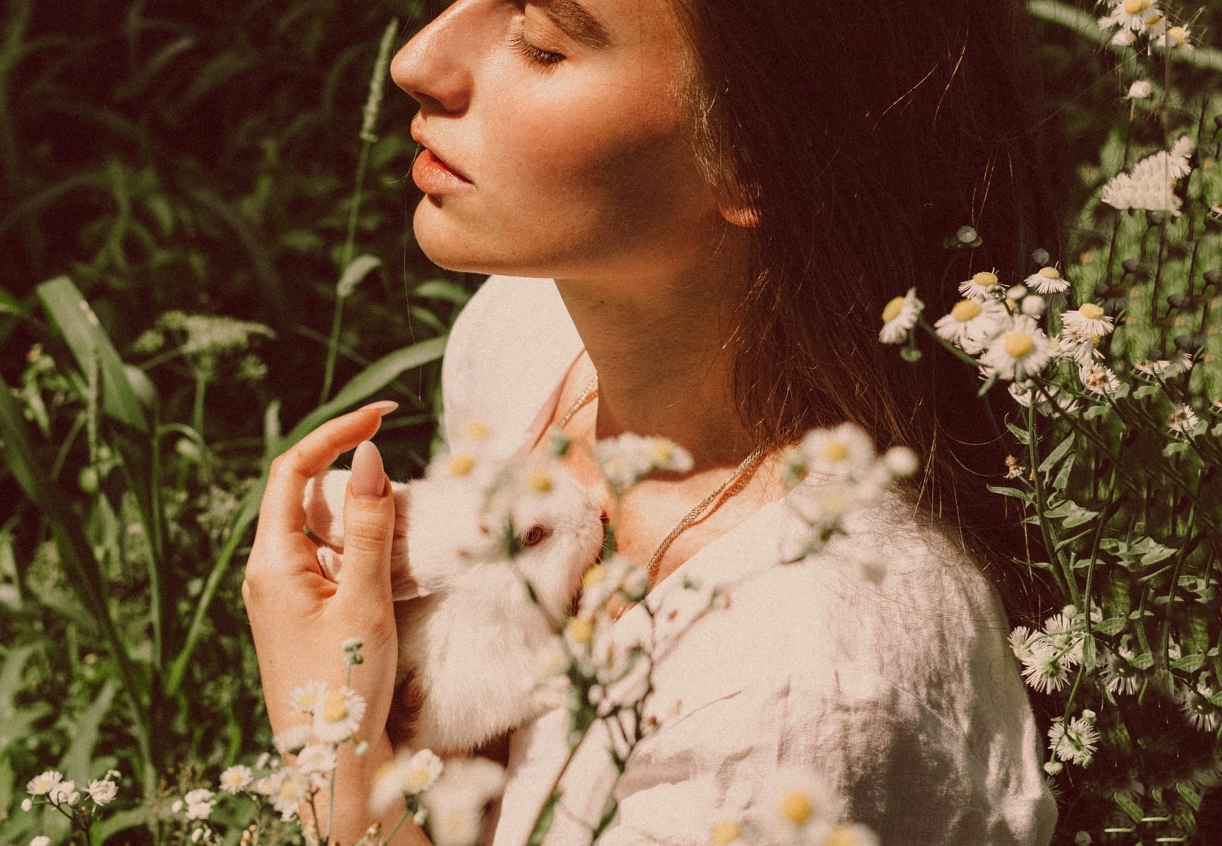 Young woman clutching bunny in field of flowers